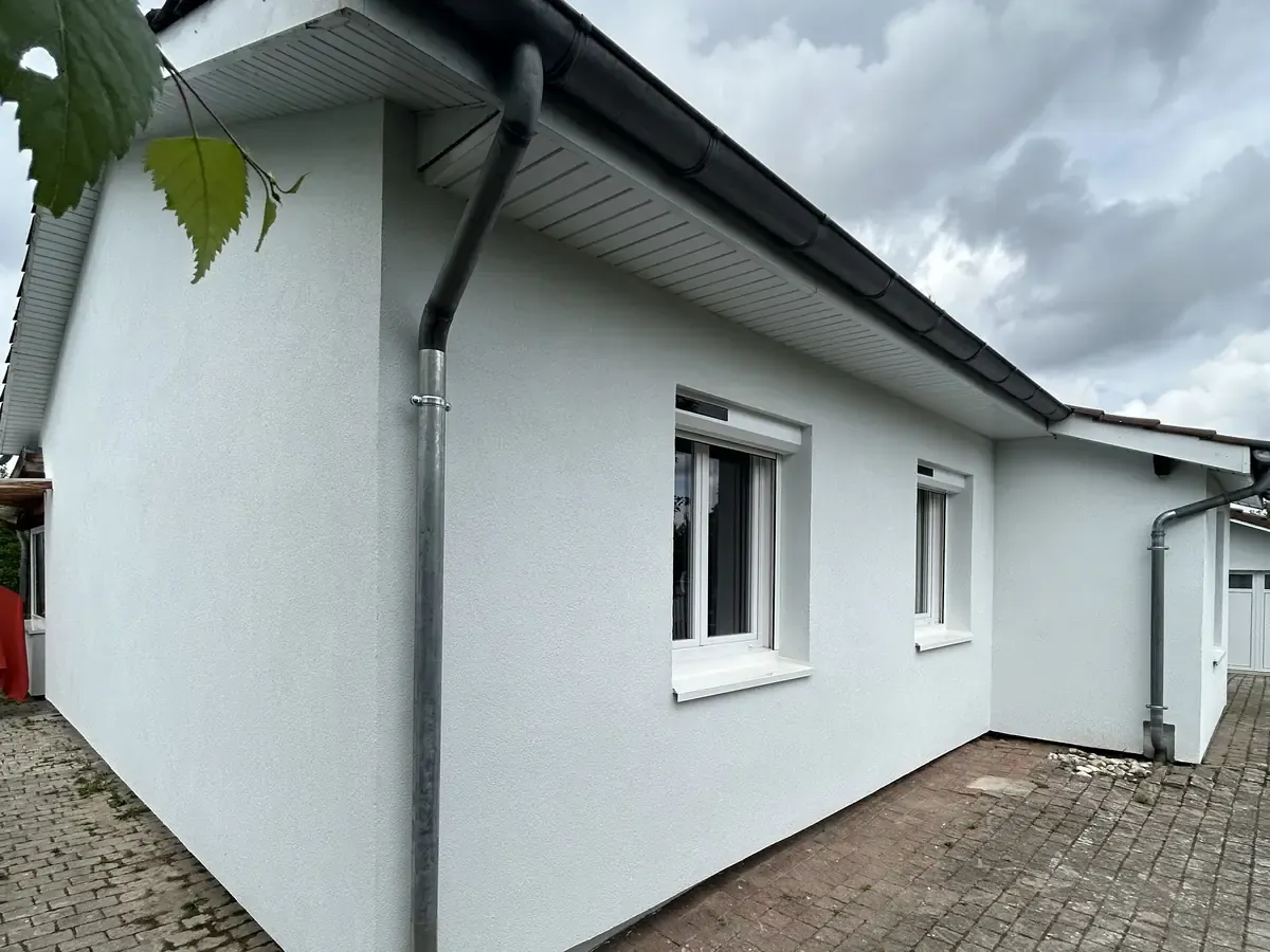 Angle d'une maison, enduit de finition blanc, gouttière et descente neuves