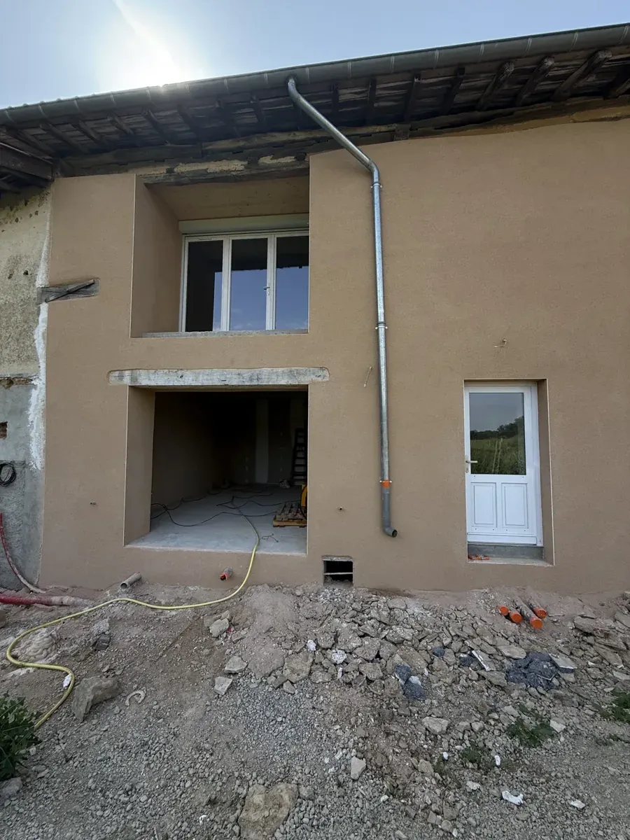 Façade de ferme en pisé fraîchement enduite en beige, ouvertures neuves