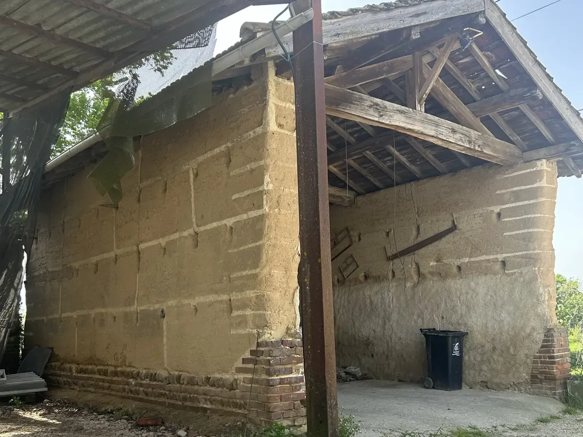 Mur en pisé à nu sous l'auvent d'une grange, avant enduit