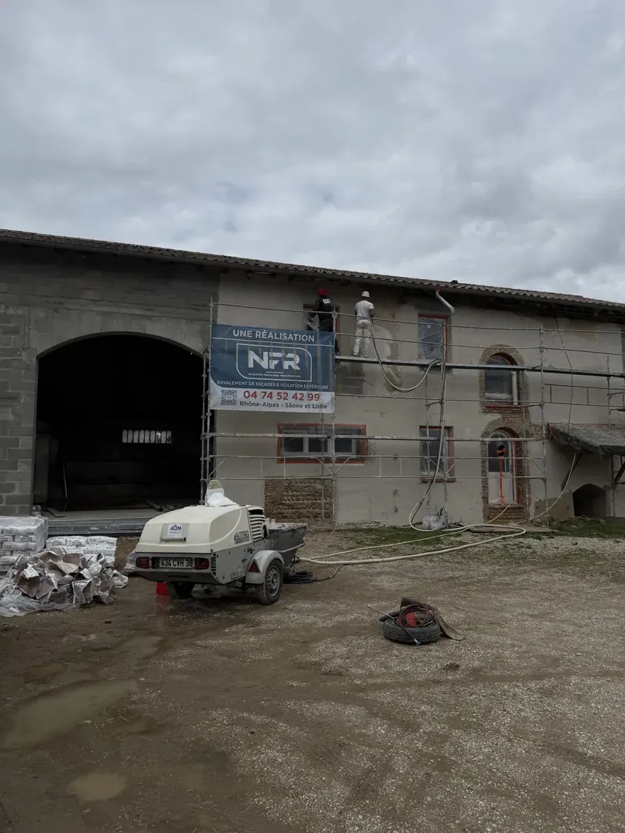 Deux compagnons NFR sur l'échafaudage projettent l'enduit sur la ferme en pisé, machine à projeter au sol