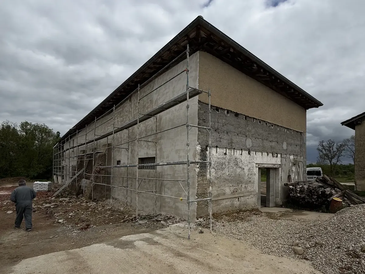 Ferme en pisé sous échafaudage, sous-enduit gris en cours d'application